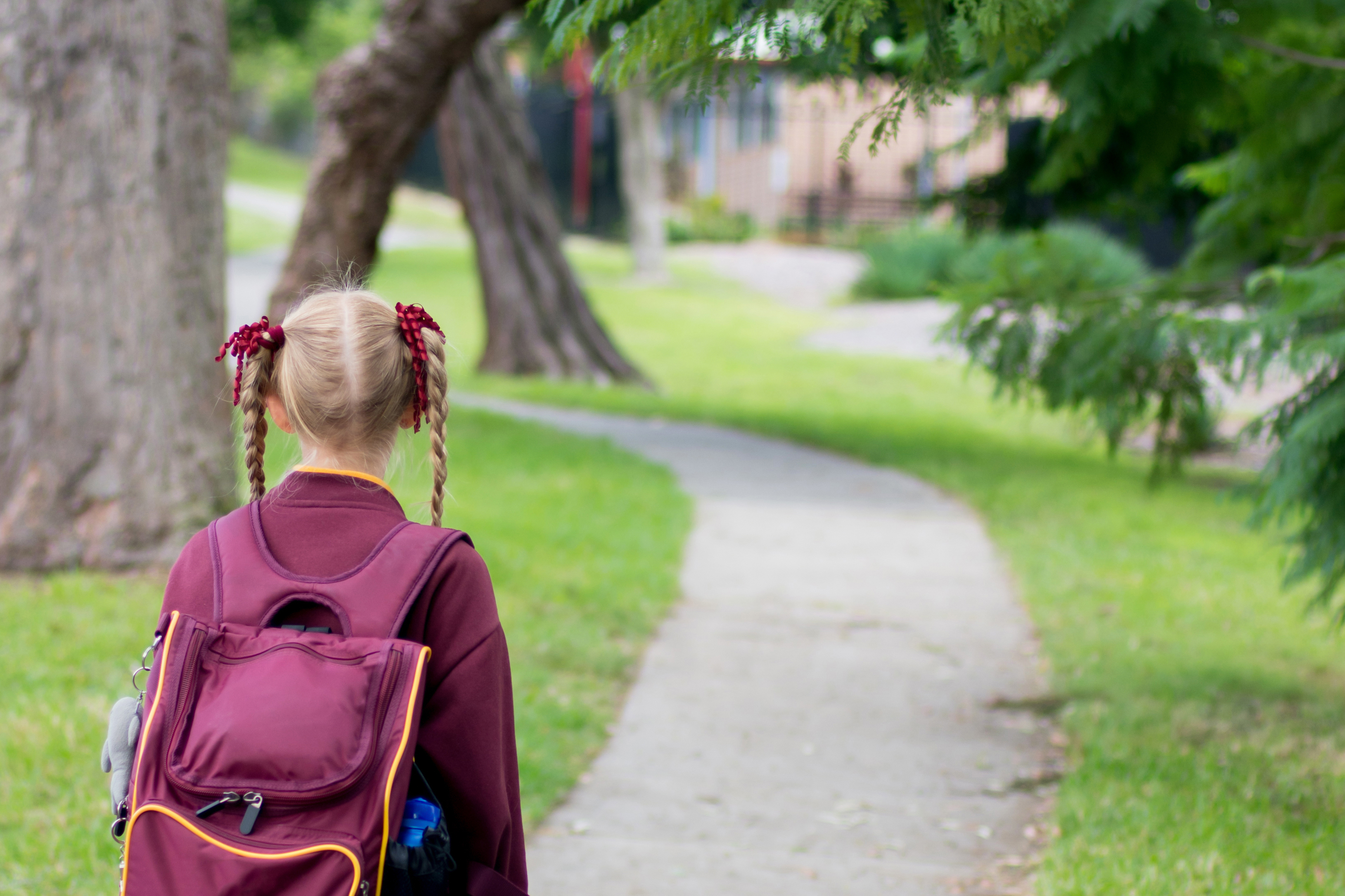 Girl in pigtails and school uniform with backpack walking home from school alone