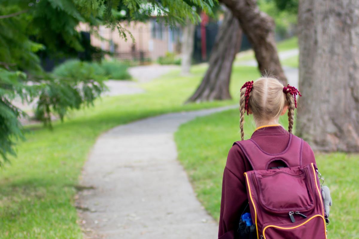 Girl in pigtails and uniform with backpack walking home from school alone