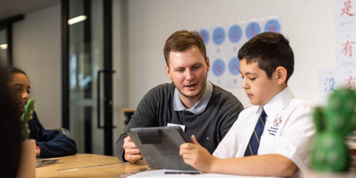 A male teacher looks at a tablet with a male student. 